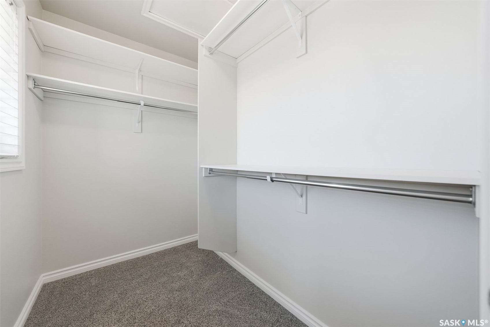 Walk-in closet with carpet flooring, white shelving, and chrome hanging rods