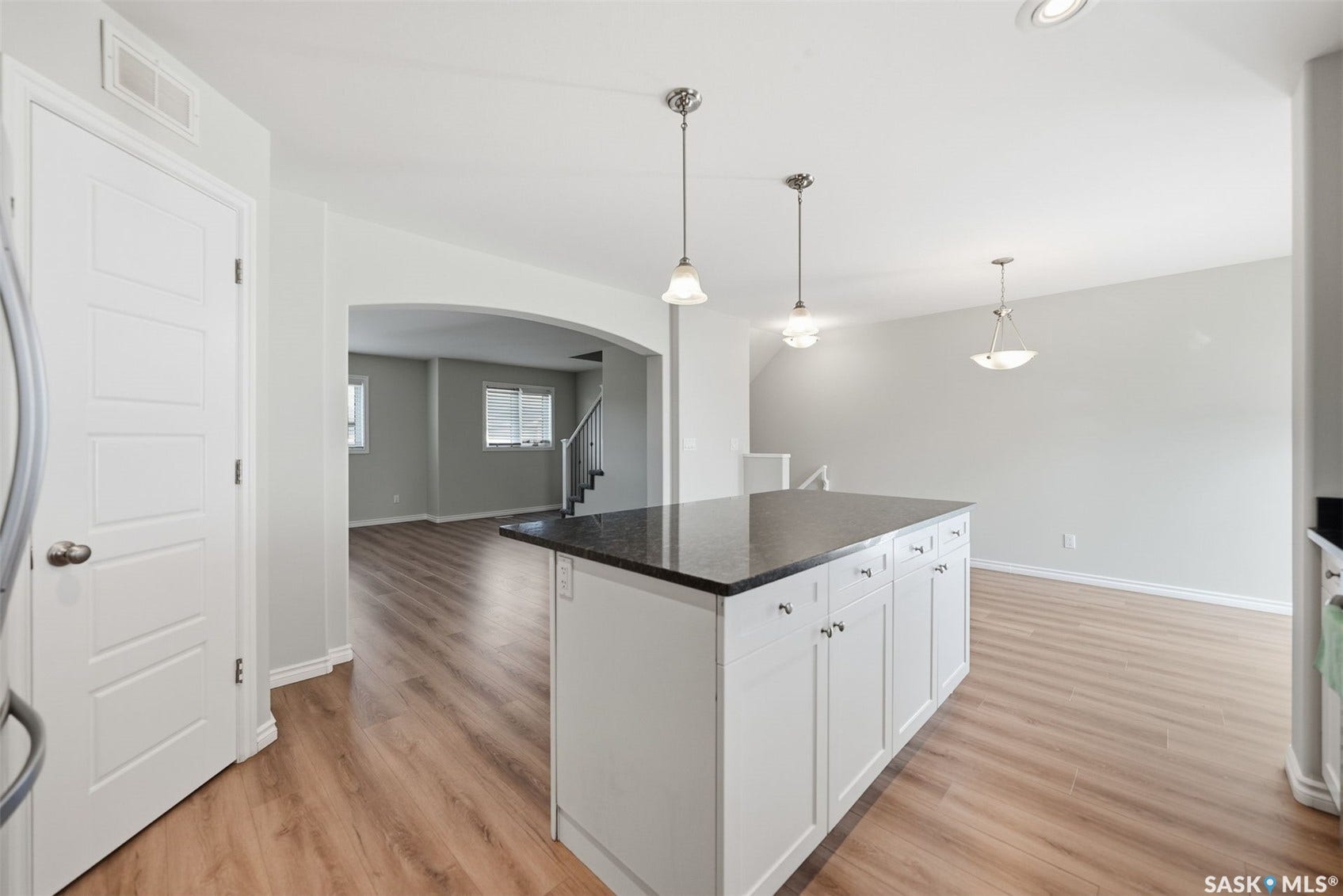 Central kitchen island with dark countertop, white cabinetry, and pendant lighting