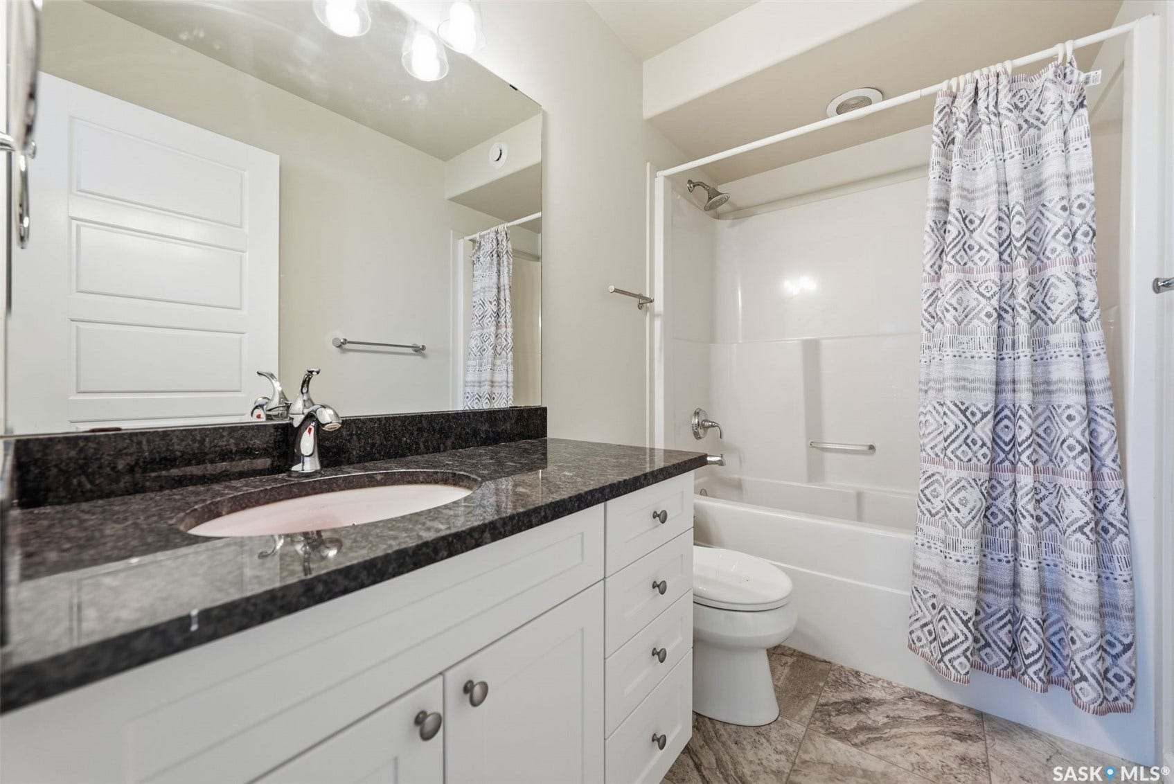 White vanity with storage, dark countertop, undermount sink with chrome faucet, full-width mirror, and a built-in shower/tub combination