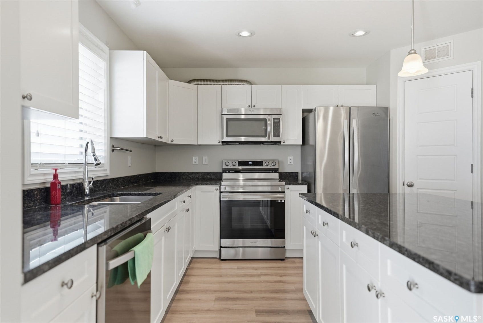 Modern kitchen featuring white cabinetry, dark stone countertops, stainless steel appliances, wood-finish flooring, and recessed lighting