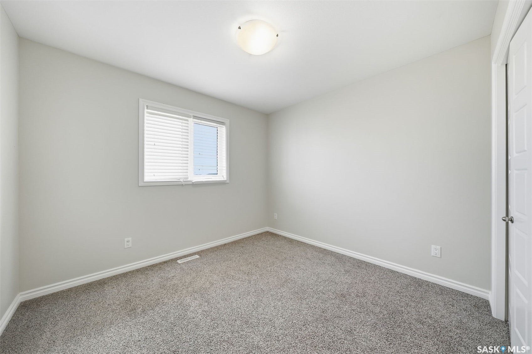 Neutral gray wall paint, gray carpet, white trim, window with blinds, and a flush-mount ceiling light