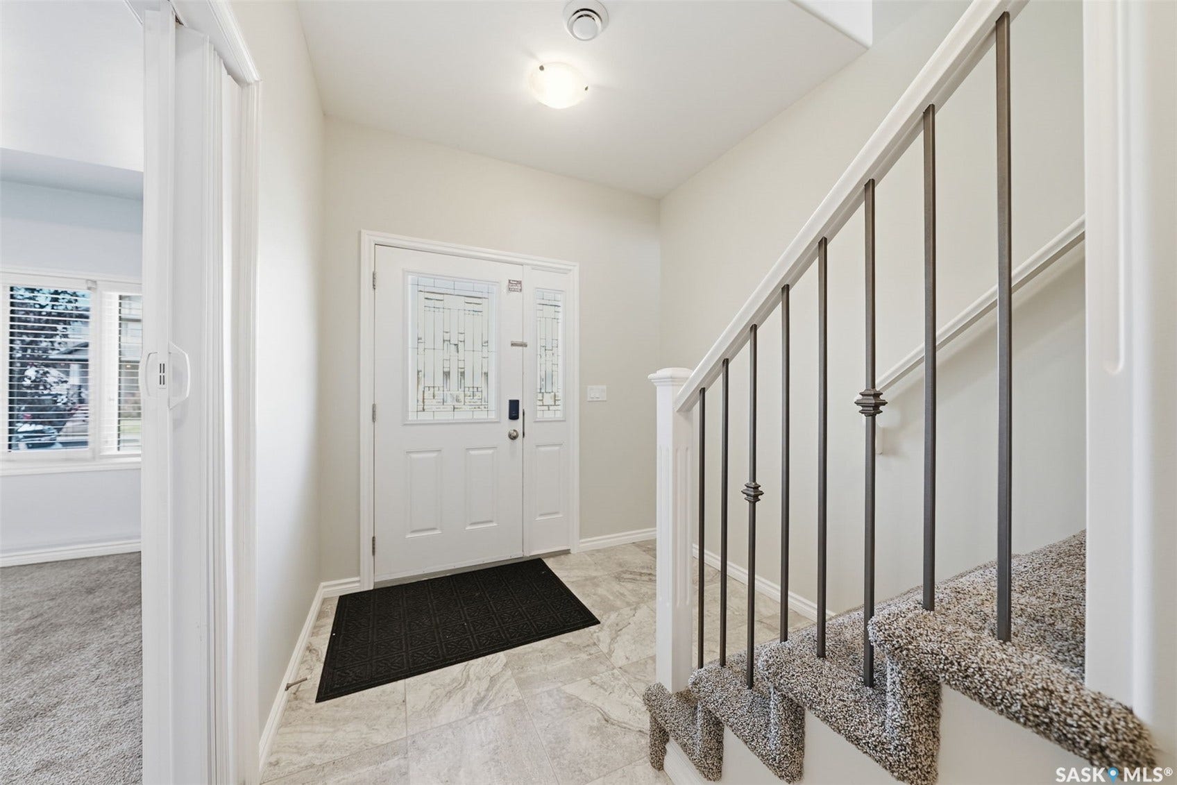 Entryway featuring a decorative glass front door, large format tile flooring, and a carpeted staircase with wrought iron balusters