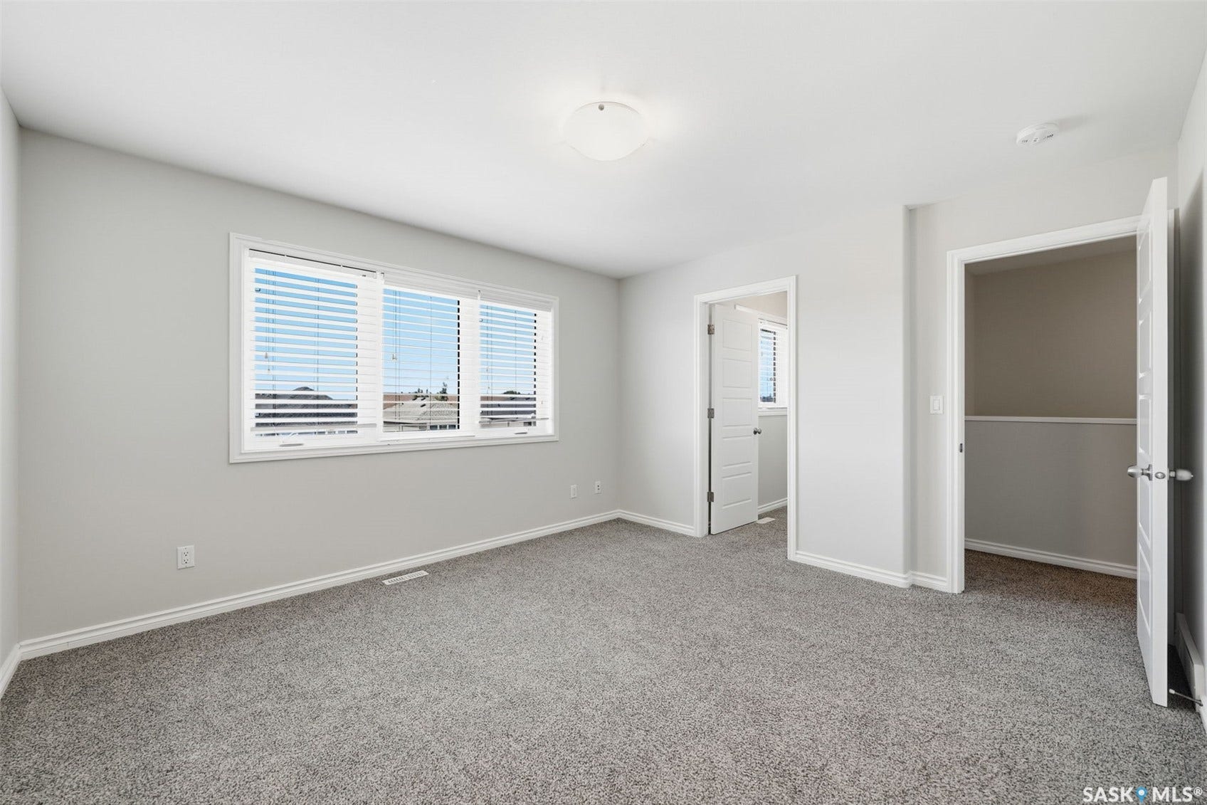 Expansive room with neutral gray carpeting, white painted walls, a large window with blinds, and white trim