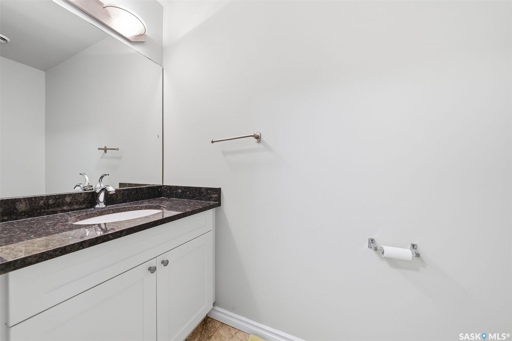 White vanity cabinetry with dual doors, under-mount sink, dark stone-finish countertop, chrome faucet, and a large wall-mounted mirror