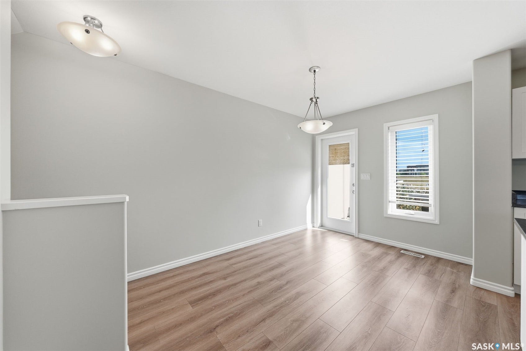 Wood-finish flooring, white trim, overhead lighting, pendant fixture, and a glass-paneled door