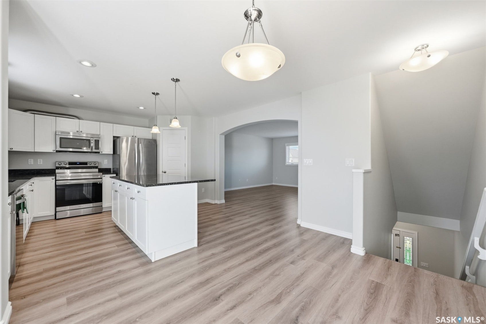Kitchen featuring white cabinetry, stainless steel appliances, dark countertops, a central island, and wood-finish flooring