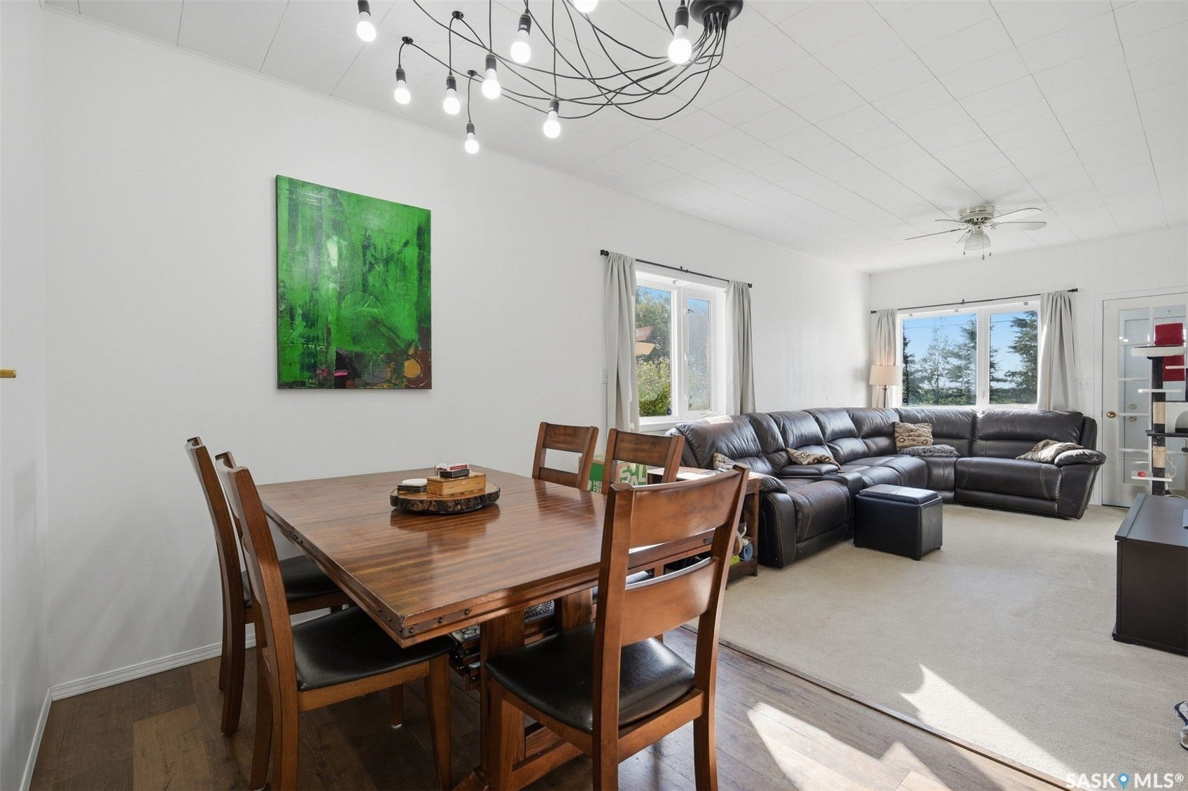Open-concept living space with wood-finish flooring, white walls, and a modern chandelier