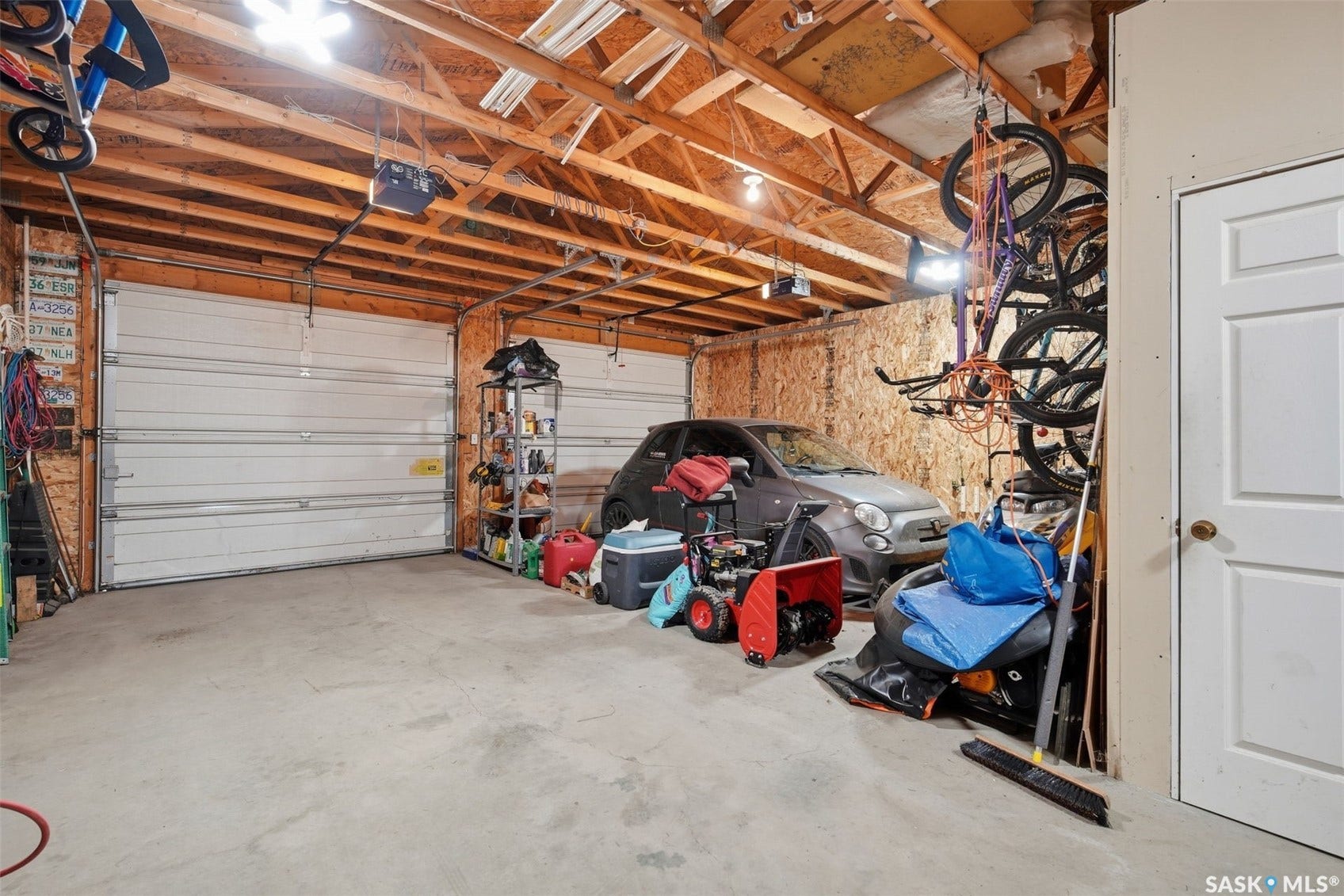 Two white roll-up garage doors, exposed wood beam ceiling, concrete flooring, and an interior access door