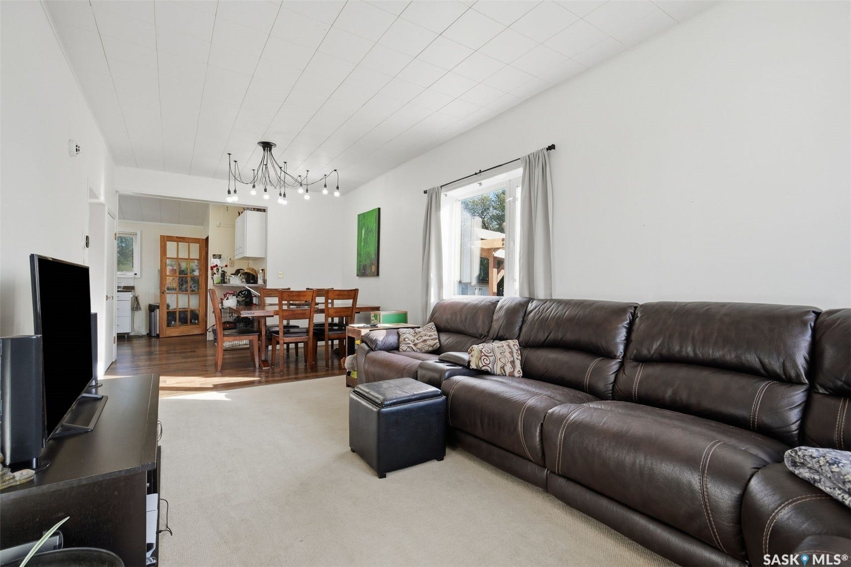 Open-concept living area featuring a neutral carpeted floor, white walls, and a large window with natural light