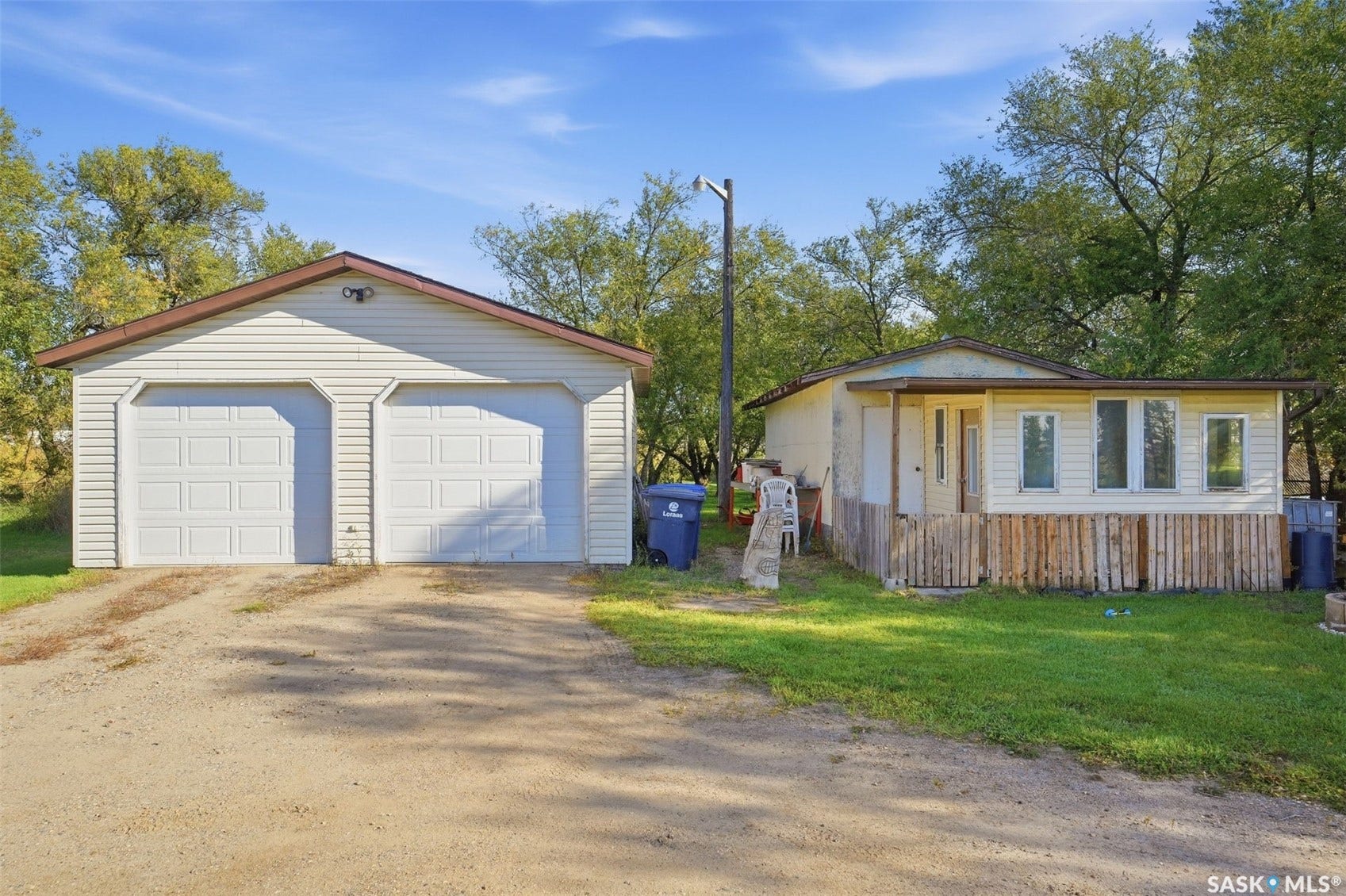 Two-car detached garage with white paneled doors, gravel driveway, and a separate structure featuring multiple windows