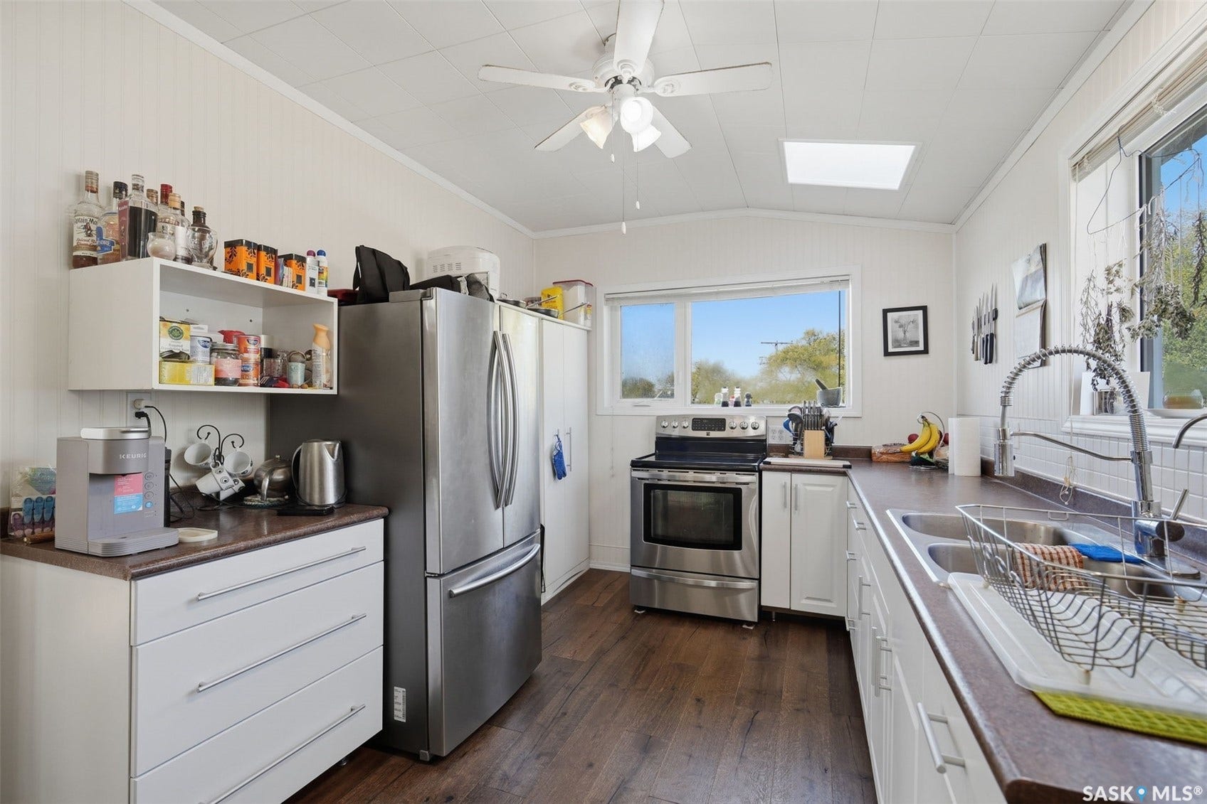 Functional kitchen featuring wood-finish flooring, white cabinetry, a skylight, and stainless steel appliances
