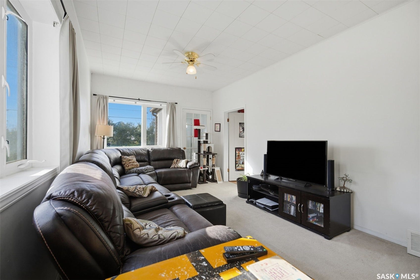Living area featuring carpet flooring, white walls, multiple windows, and a ceiling fan with integrated lighting
