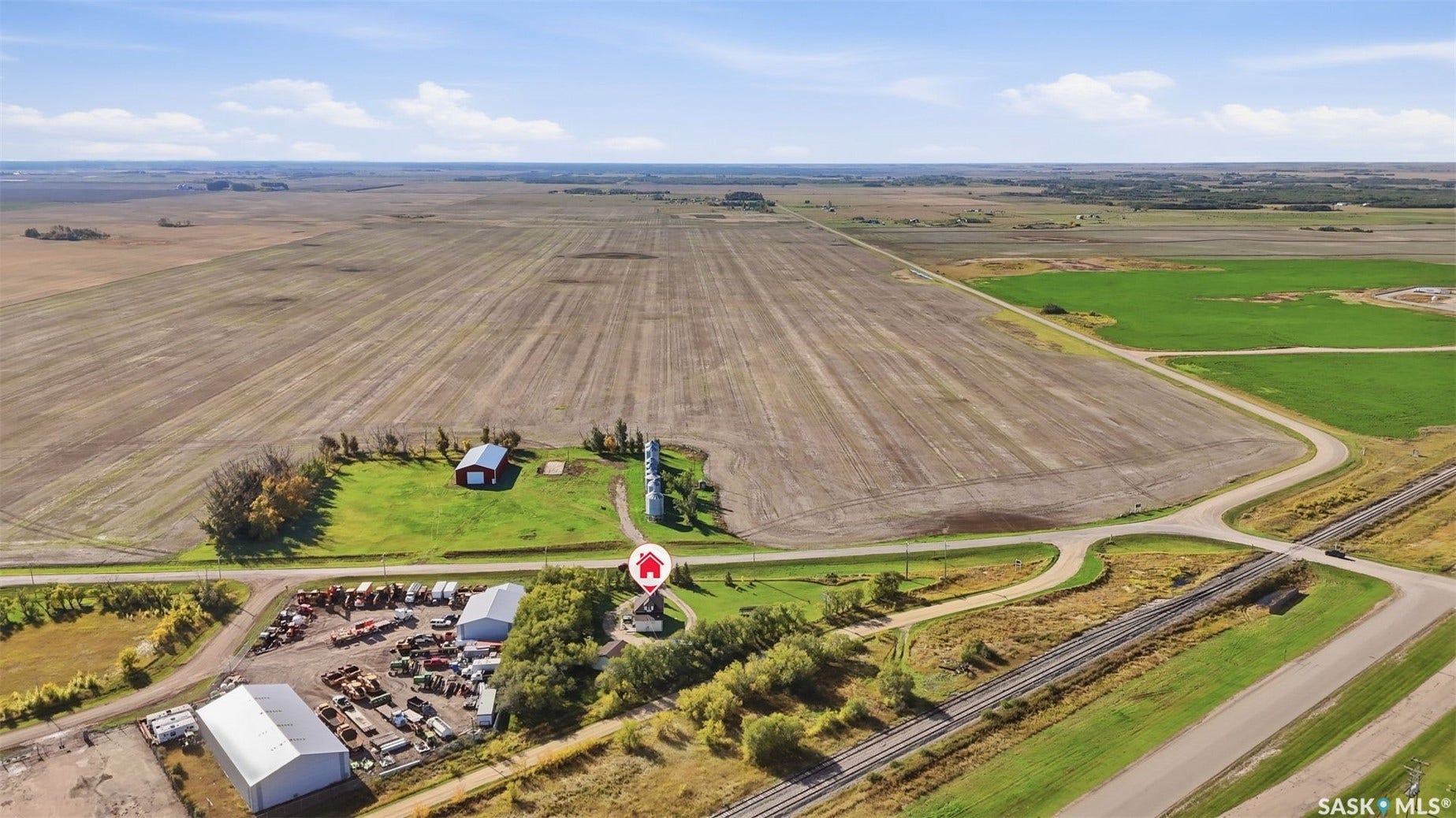 Expansive agricultural landscape with cultivated fields, multiple outbuildings, and a railroad crossing