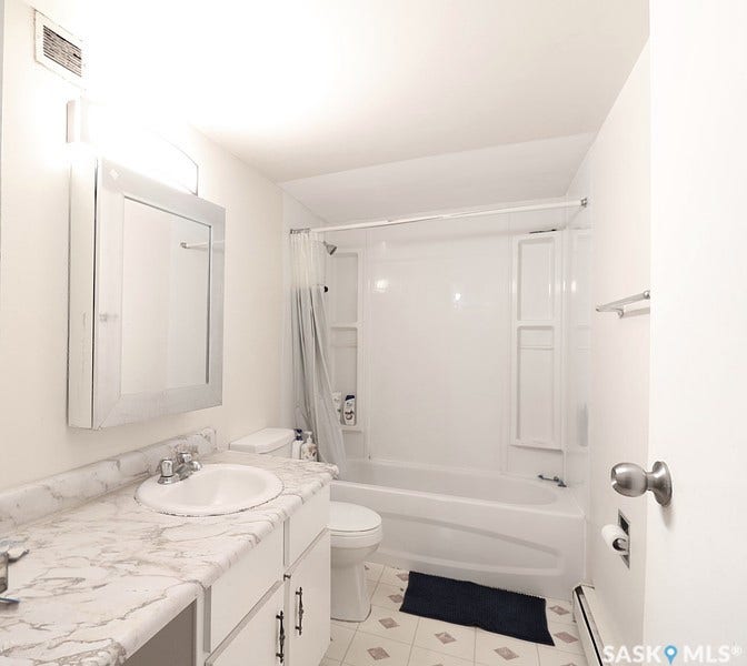 White vanity with a single basin sink, wall-mounted mirror, and a white bathtub with a shower kit