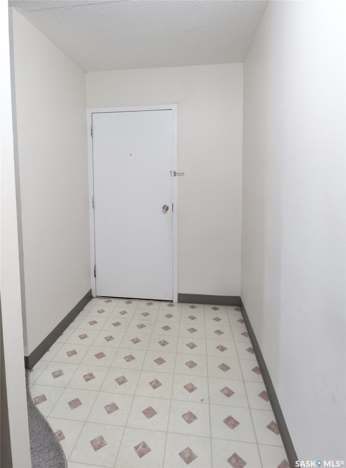 White interior door with polished hardware, textured ceiling, and patterned tile flooring