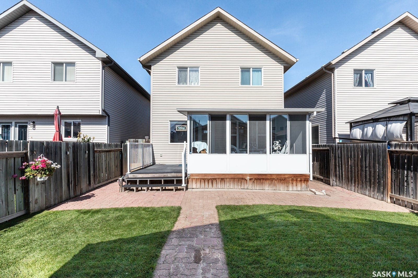 Manicured lawn with a paver walkway, leading to a screened-in sunroom and a wood deck