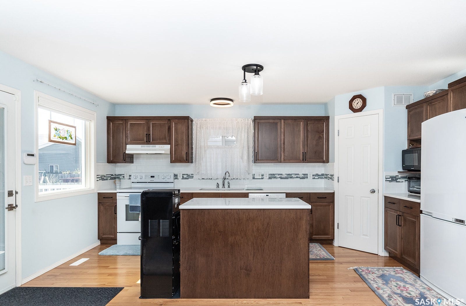 Kitchen featuring hardwood flooring, dark wood cabinetry, a center island, quartz countertop, corner pantry, and white appliances