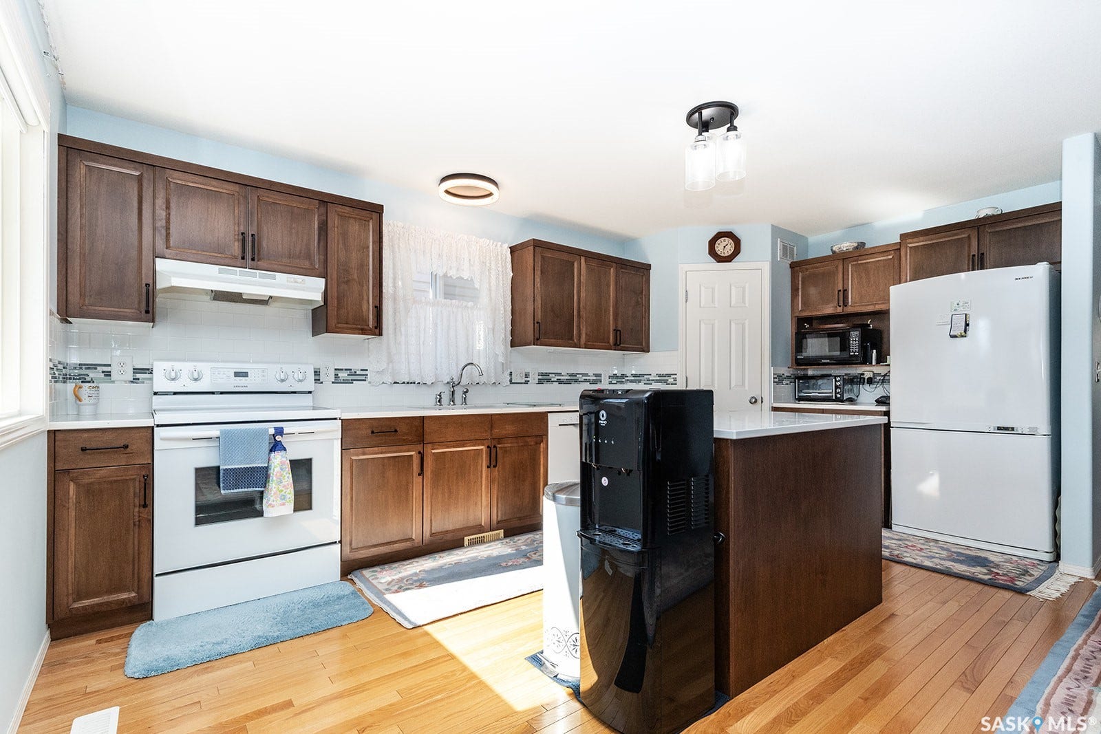 Kitchen featuring wood-finish cabinetry, quartz countertops, hardwood flooring, and a central island