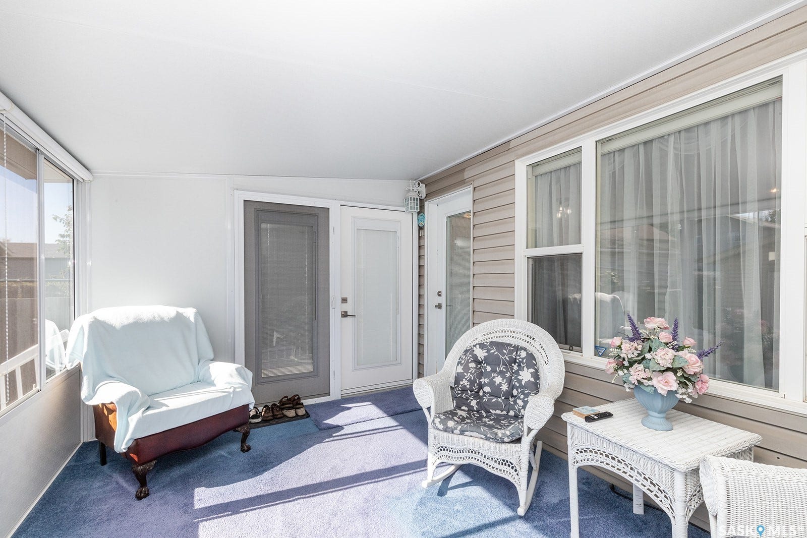 Enclosed sun room featuring a solid roof, large windows, and an exterior door with a screen door