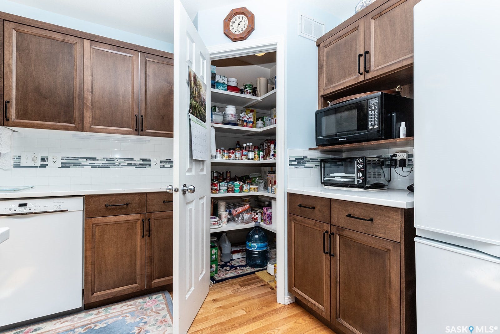 Kitchen featuring hardwood flooring, dark wood cabinetry, quartz countertop, and a walk-in pantry with shelving