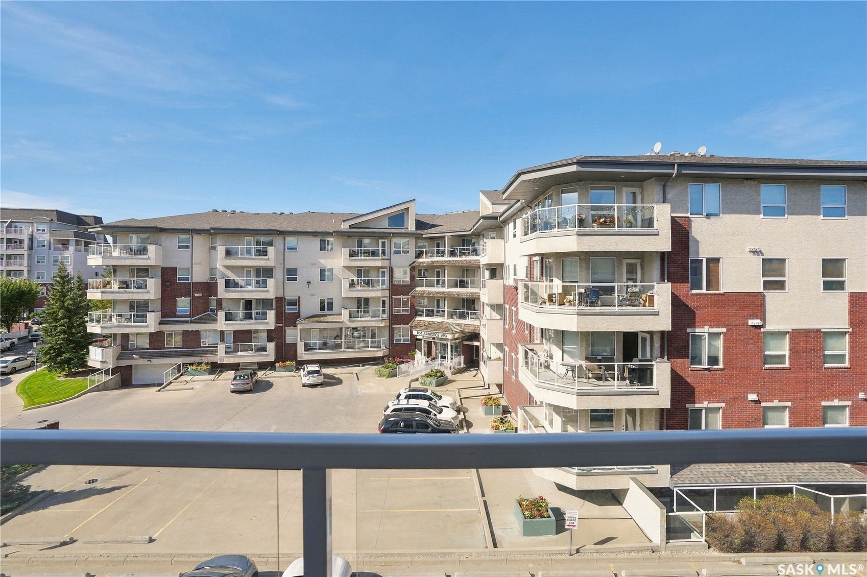 Multi-story building featuring a brick and stucco exterior, multiple balconies with glass railings, and an on-site parking area