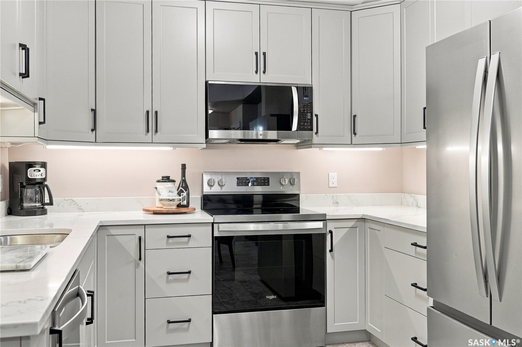 White shaker-style cabinetry with black hardware, white countertops, built-in microwave, stainless steel oven, and stainless steel refrigerator