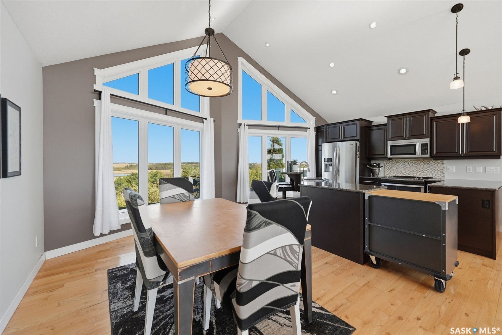 Vaulted ceiling with transom windows, recessed lighting, wood-finish flooring, dark wood cabinetry, and stainless steel appliances