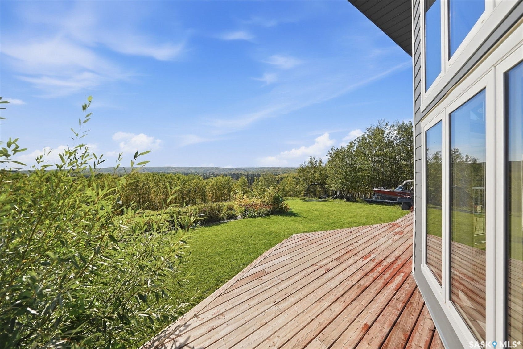 Expansive outdoor deck with a natural wood finish, multi-pane windows, and a manicured lawn surrounded by mature trees