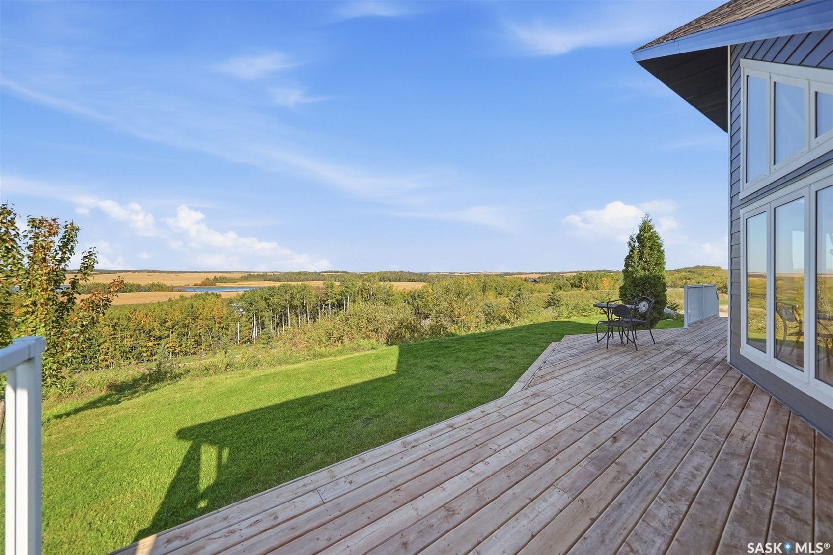 Expansive wood deck with a sloped lawn area and mature trees