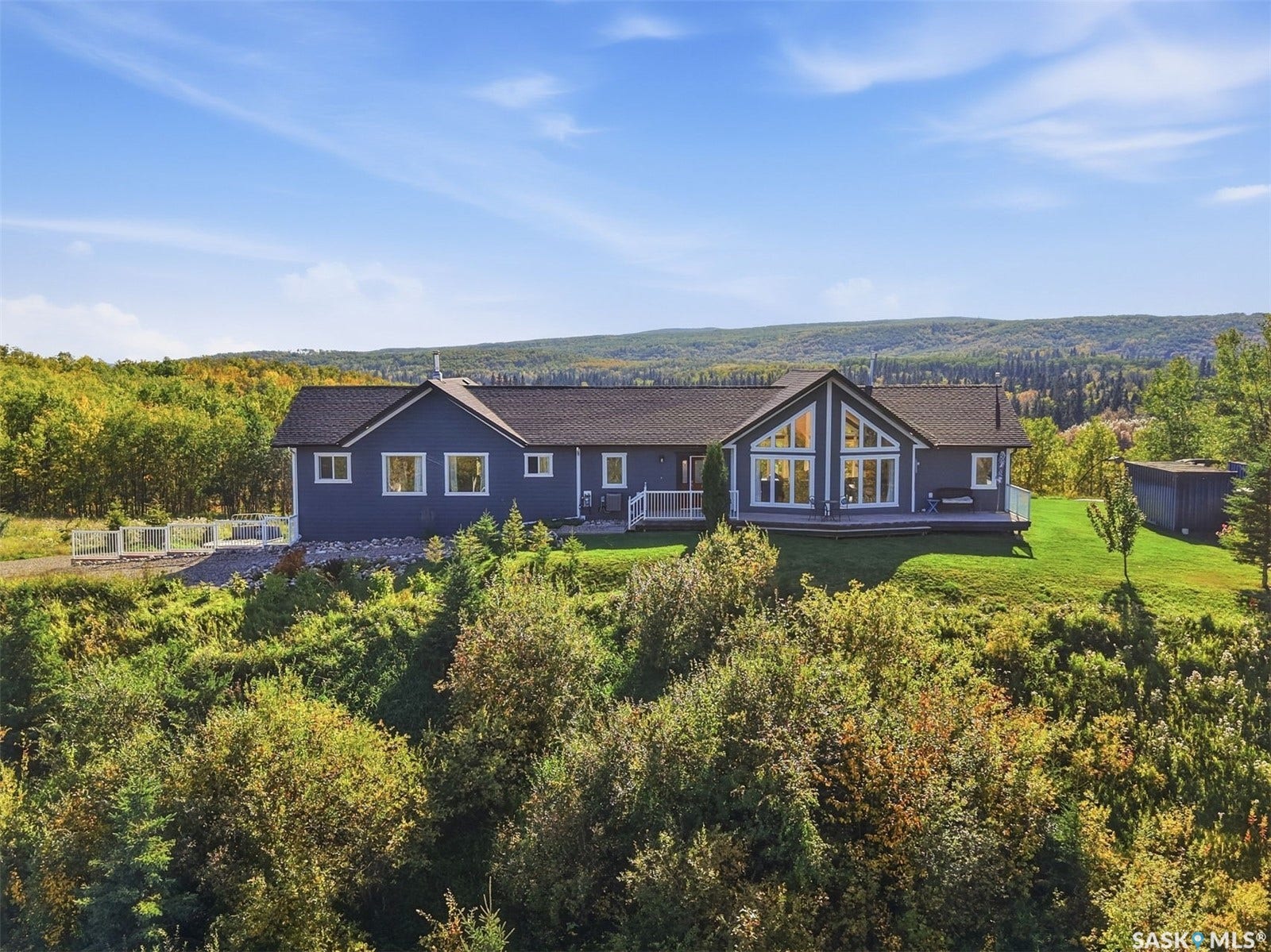 Spacious residence with dark blue siding, a dark shingled roof, and multiple large windows