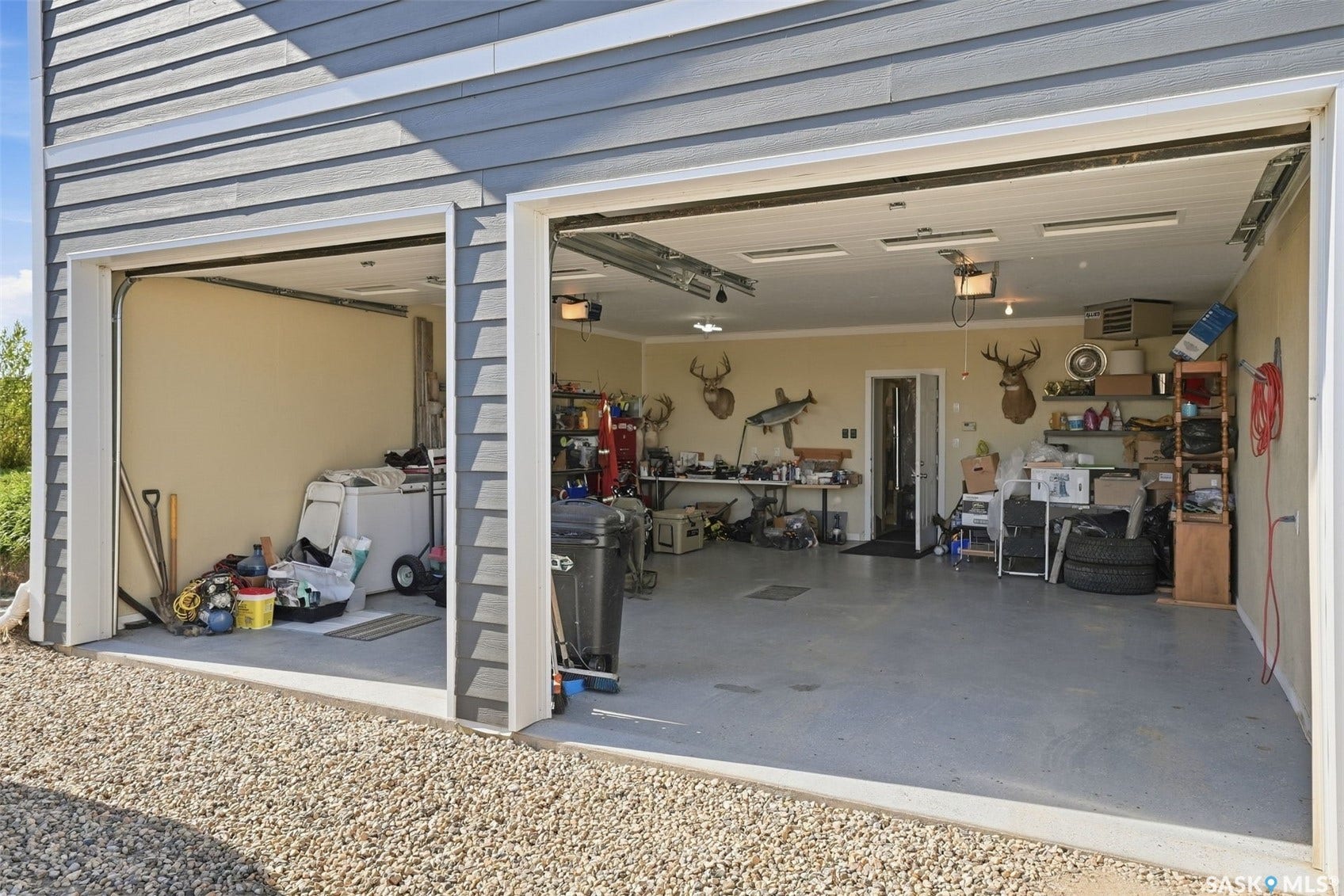Two-car garage with gray siding, two overhead doors, and a gravel foreground