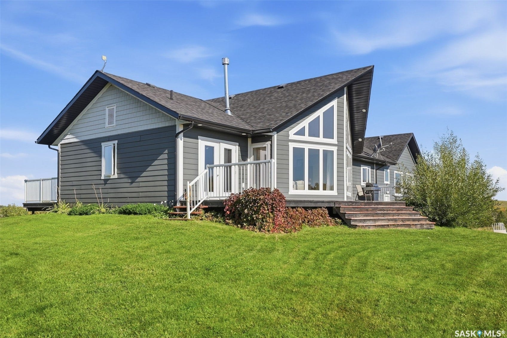 Contemporary exterior with dark gray siding, light gray gable siding, expansive A-frame windows, a white-railed deck, and a wood-stepped patio