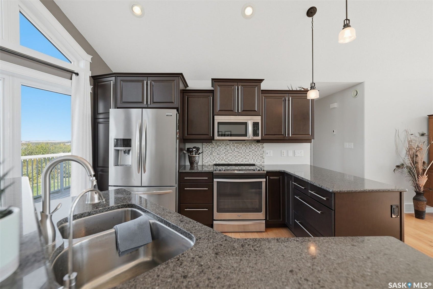 Kitchen featuring dark wood cabinetry, stainless steel appliances, speckled countertops, mosaic tile backsplash, and a double basin sink with a gooseneck faucet