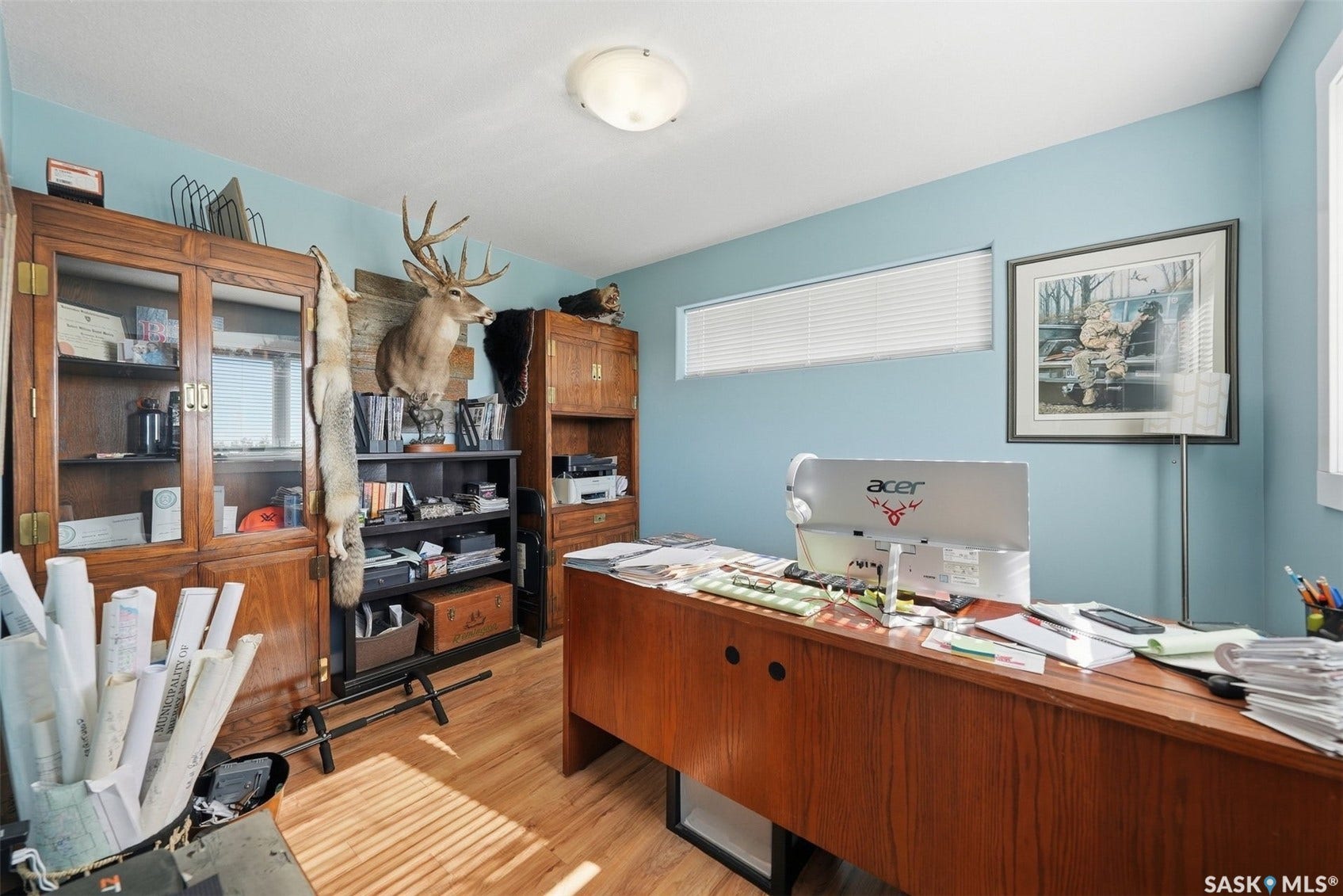 Wood-finish flooring, built-in shelving, wood-finish cabinetry with glass panels, light blue wall paint, and a horizontal window with blinds
