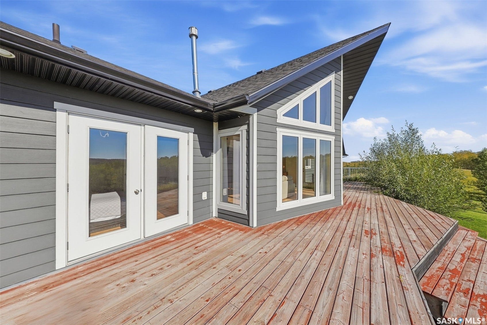 Expansive wood deck with multiple levels, featuring double glass-paneled doors and large windows