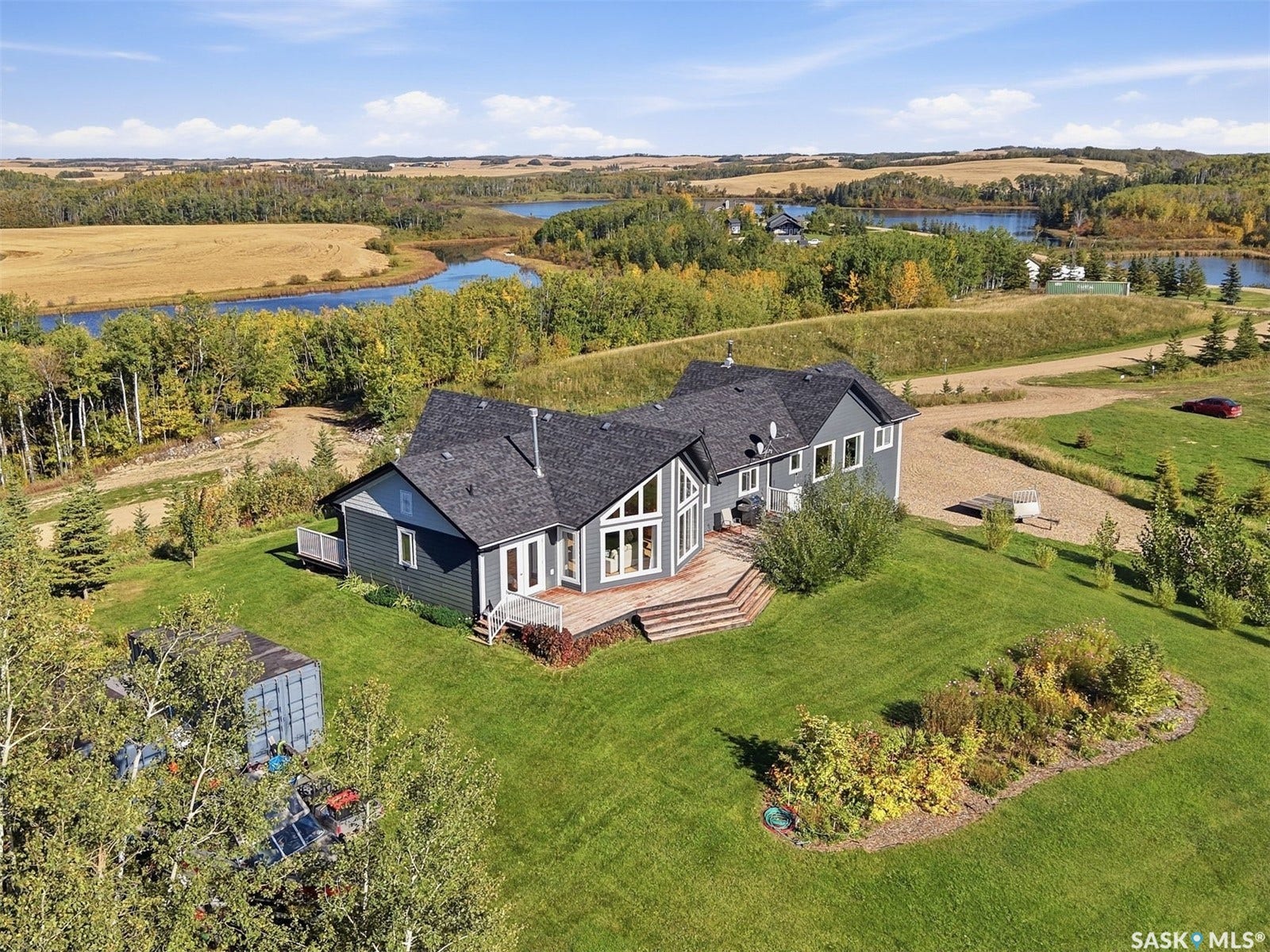 Expansive property featuring a grey-sided residence with multiple windows and a dark shingled roof