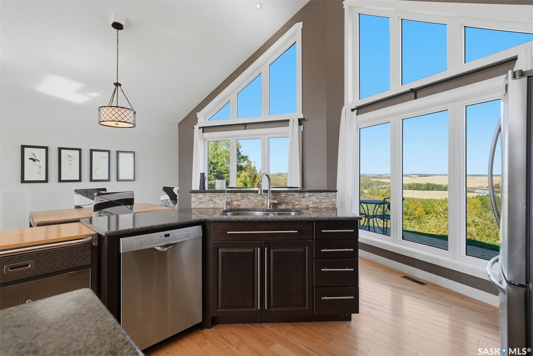 Vaulted ceiling with a contemporary chandelier, stainless steel dishwasher, wood-finish flooring, and expansive windows