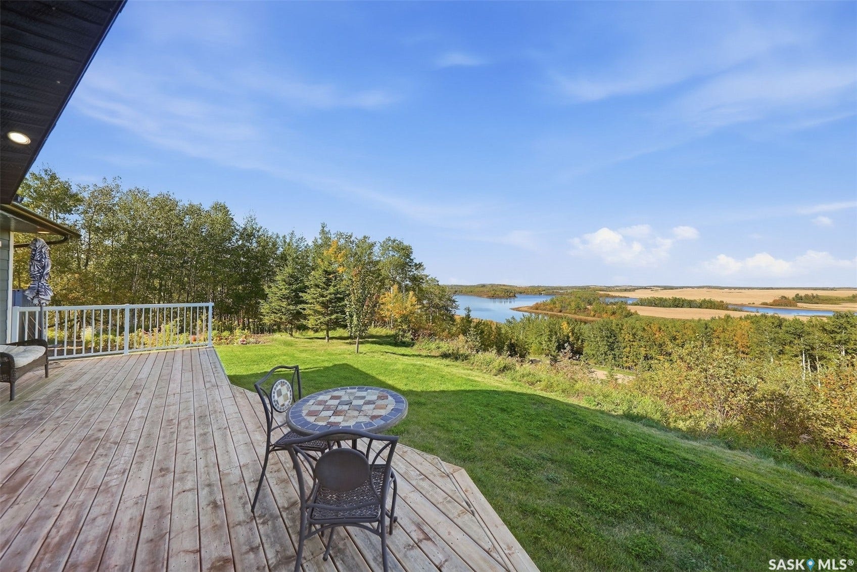 Expansive outdoor deck with wood planking and white railing, overlooking a sloped lawn and distant water body