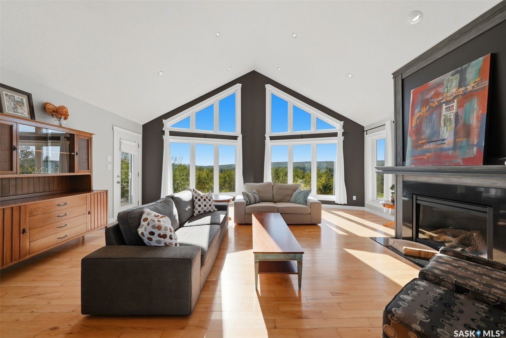 Vaulted ceiling with recessed lighting, expansive picture windows, wood-finish flooring, built-in fireplace, and a built-in display cabinet