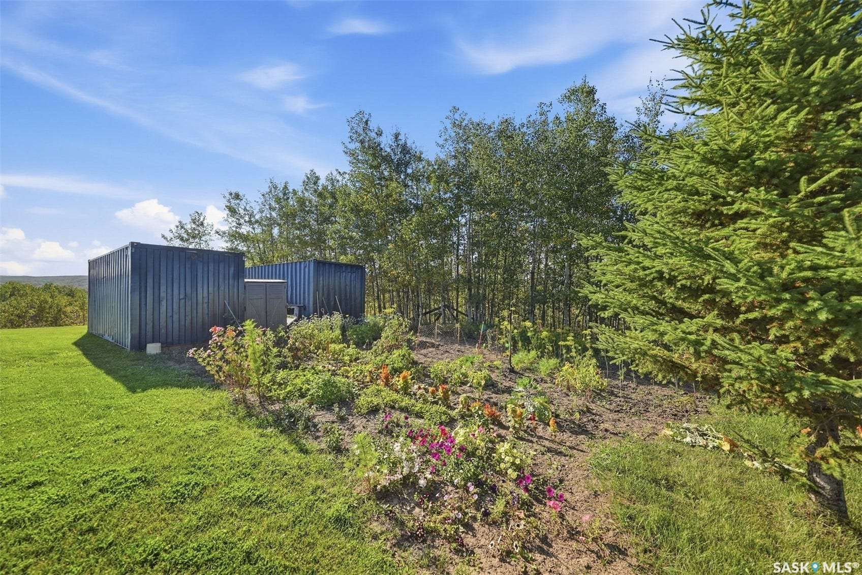 Two storage containers on a grassy expanse, bordered by a garden bed and mature trees
