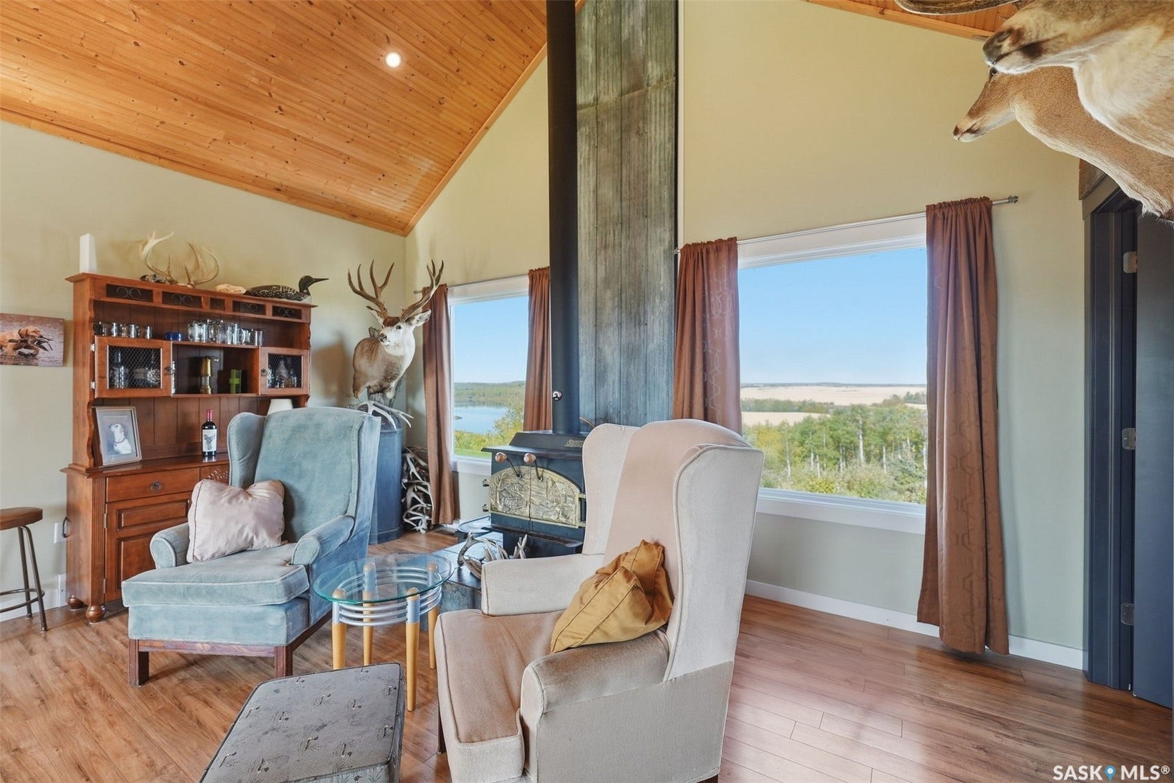 Vaulted wood-paneled ceiling, wood-finish flooring, built-in wood cabinetry, wood-burning stove with a metal flue, and expansive windows