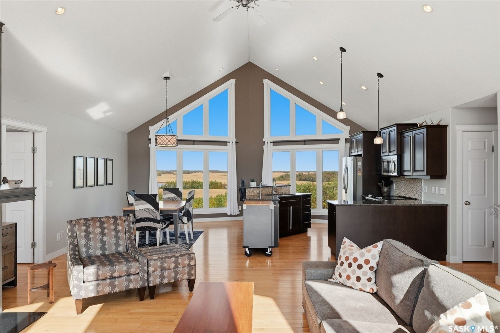 Vaulted ceilings, wood-finish flooring, recessed lighting, expansive windows, and a kitchen featuring dark wood cabinetry
