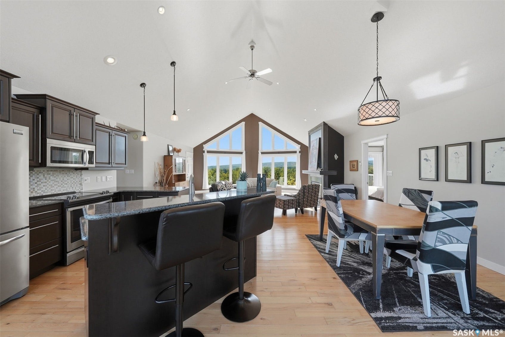Vaulted ceilings with recessed lighting, integrated kitchen island, stainless steel appliances, and wood-finish flooring