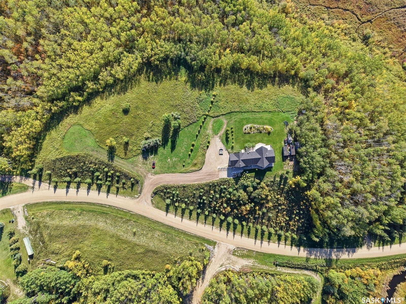 Expansive property featuring a single-story residence, gravel driveway, and surrounding forested areas