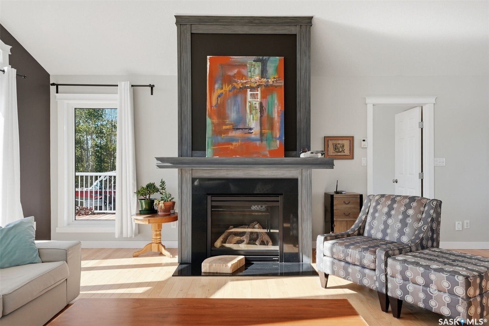 Hardwood flooring, a prominent fireplace with a dark tile surround, a built-in mantel, and a window with white trim