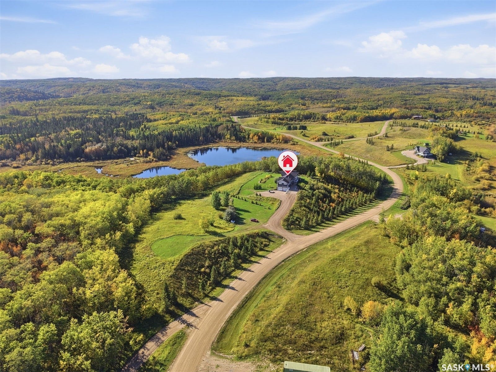 Expansive landscape featuring rolling hills, mature trees, a visible pond, and a winding dirt road leading to the property