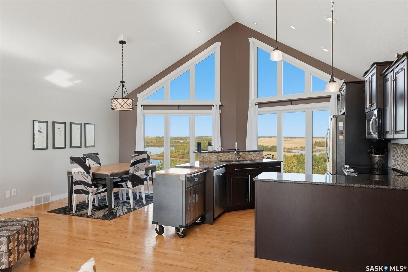 Vaulted ceilings with large triangular windows, hardwood flooring, dark wood cabinetry, and stainless steel appliances