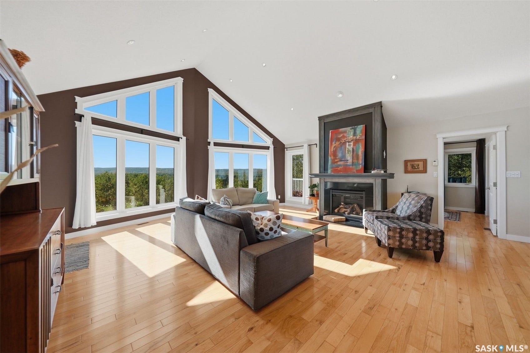 Vaulted ceilings with recessed lighting, expansive windows, light wood-finish flooring, and a stone-clad fireplace with mantel