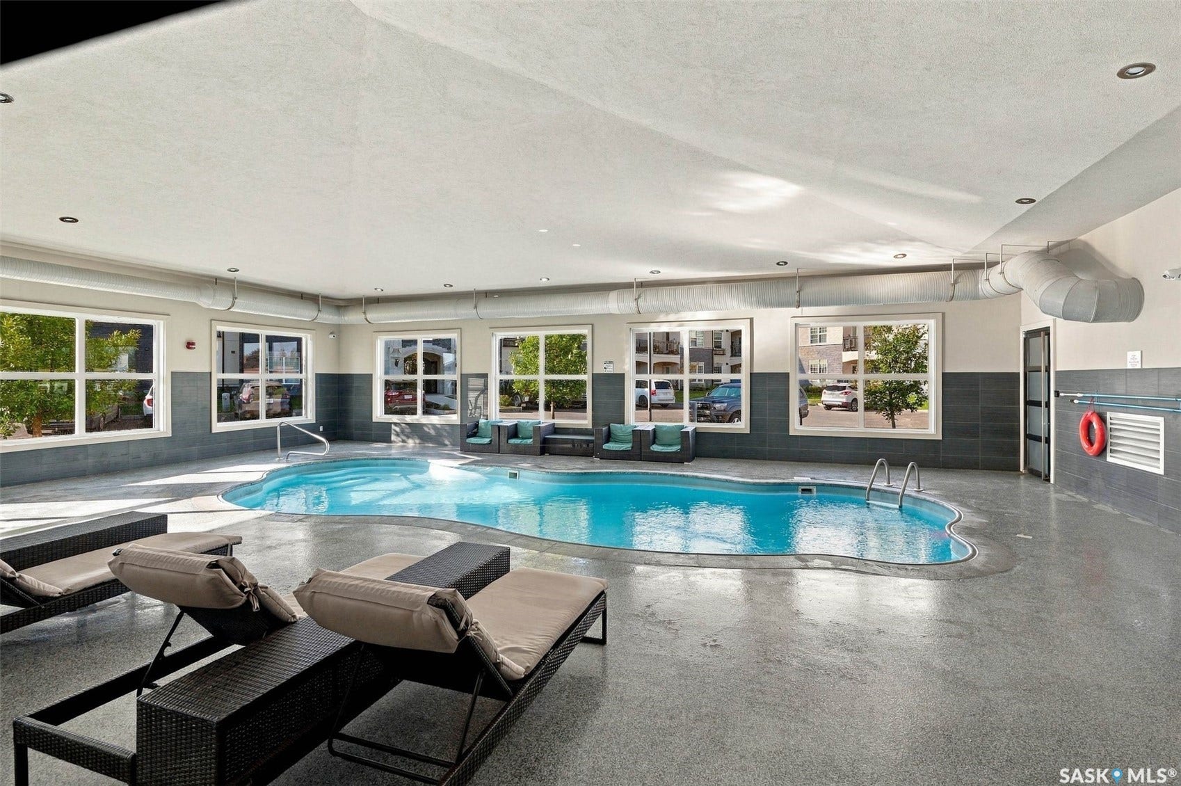 Indoor swimming pool with an irregular shape, surrounded by large windows, recessed lighting, and a grey tile accent wall
