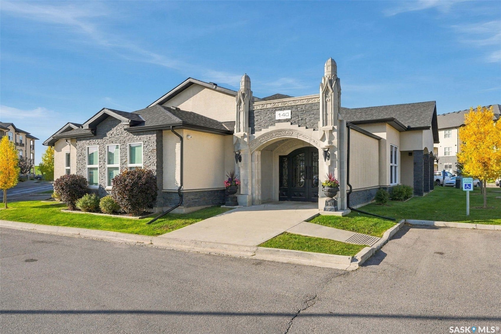 Stucco and stone facade with arched entry, gabled roofline, and established landscaping